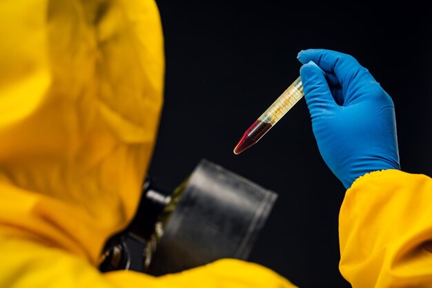 Foto un médico o biólogo masculino que usa un traje protector para combatir una pandemia o un coronavirus. está sosteniendo un tubo de ensayo.