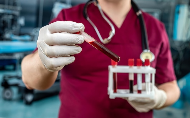 El médico o bioquímico masculino usa guantes de uniforme rojo de la enfermedad del virus examina la sangre en un tubo de ensayo en un hospital moderno