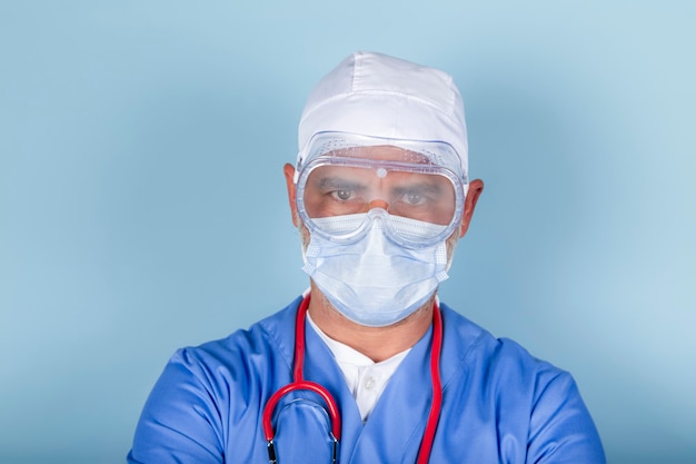 Médico o enfermera con máscara protectora y gafas médicas sobre una superficie azul