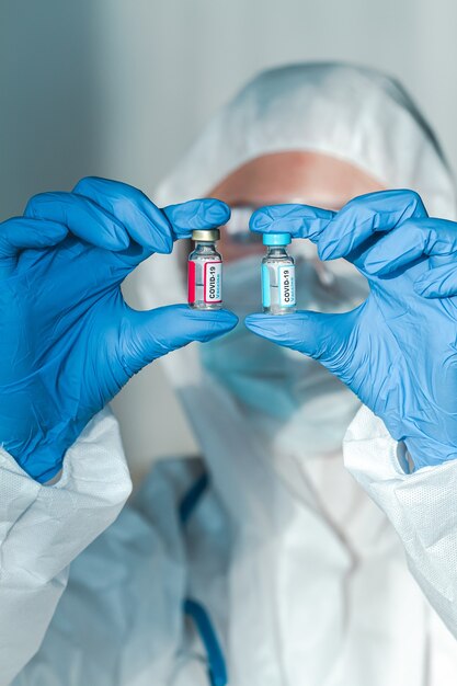 Médico o enfermera con un traje de protección con una vacuna covid 19 de dos componentes en las manos