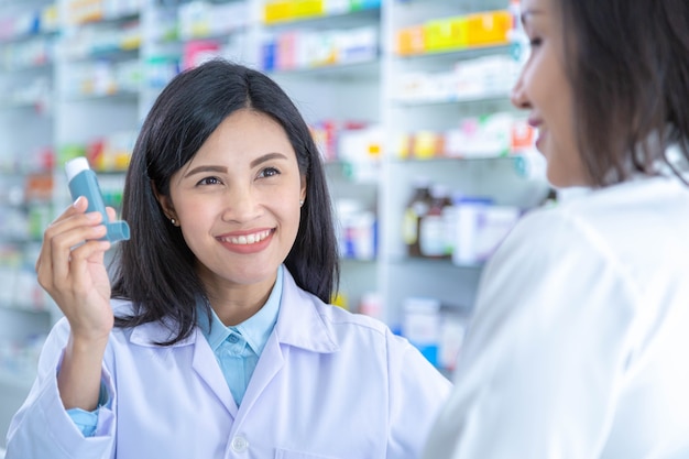 El médico o farmacéutico asiático explica cómo usar la medicina inhaladora, la clínica del asma, la enfermedad de los ancianos, ella sostiene la medicina inhaladora con la mano.