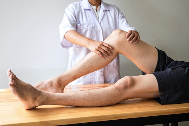 Médico o fisioterapeuta que trabaja examinando el tratamiento de la pierna lesionada del paciente masculino atleta, haciendo el dolor de la terapia de rehabilitación en la clínica.