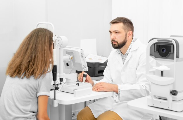 Médico oftalmologista segurando equipamento examinando olhos de meninas adolescentes na clínica