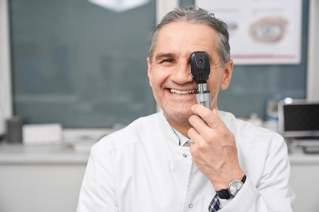 Médico optometrista sorrindo, posando, segurando o dispositivo de teste do olho.