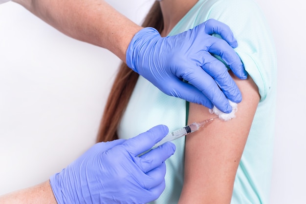 Médico ou enfermeira administrando vacina injetável em paciente jovem adolescente no ombro da vacina