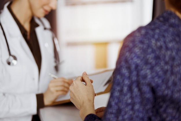 Médico y paciente discutiendo el examen de salud actual mientras están sentados en la clínica soleada. Servicio médico perfecto en el hospital.