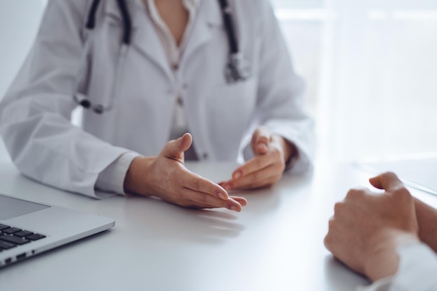 Foto médico y paciente discutiendo el examen de salud actual mientras están sentados en el escritorio en la oficina de la clínica, primer plano. concepto de medicina