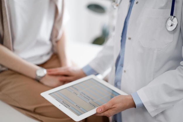 Médico y paciente discutiendo los resultados del examen de salud Médico amigable tranquilizando a una mujer joven con una mano mientras mantiene la tableta en otra concepto de medicina