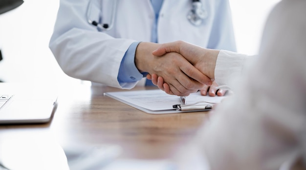Médico y paciente estrechando la mano sobre la mesa de madera en la clínica. concepto de medicina