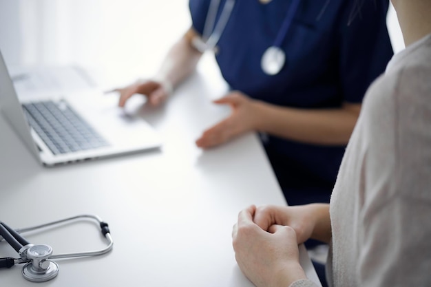 Médico y paciente hablando entre sí durante el examen de salud actual mientras están sentados en el escritorio de la clínica, primer plano de la mano. Concepto de medicina y servicio médico perfecto