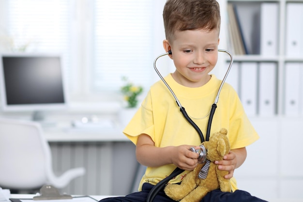 Foto médico y paciente en el hospital niño feliz divirtiéndose mientras lo examinan con estetoscopio concepto de atención médica y seguro