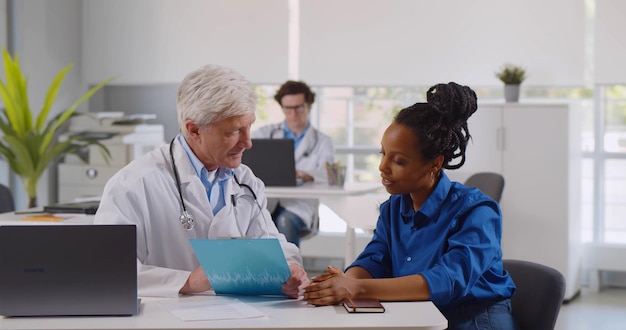 Médico y paciente mujer discutiendo el tratamiento o datos de registros médicos en el centro de diagnóstico moderno