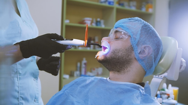 Médico y paciente con retractor en el consultorio dental pantalla protectora ultravioleta y naranja