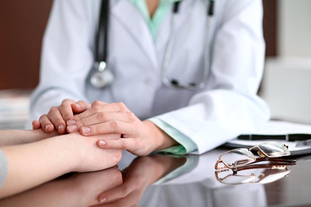 Foto médico y paciente sentados en el escritorio cerca de la ventana del hospital