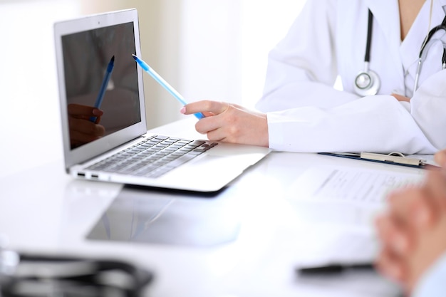 Médico y una pareja joven de pacientes discutiendo algo en la mesa. Primer plano de las manos.