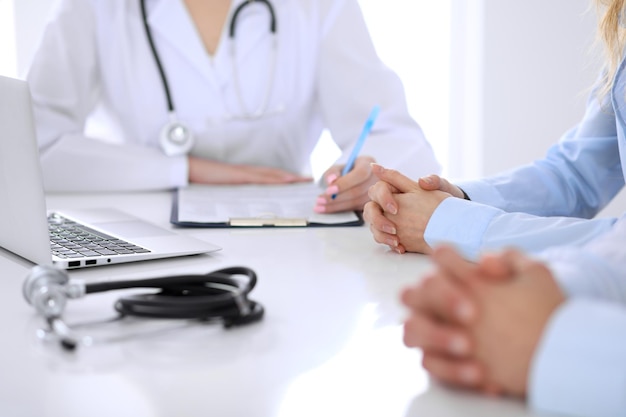 Médico y una pareja joven de pacientes discutiendo algo en la mesa. Primer plano de las manos.