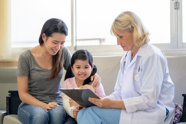 Médico pediatra examinando menina asiática com braço quebrado usando gesso no hospital