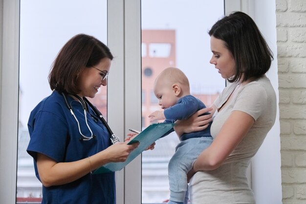 Médico pediatra hablando con la joven madre sosteniendo a su bebé en sus brazos.