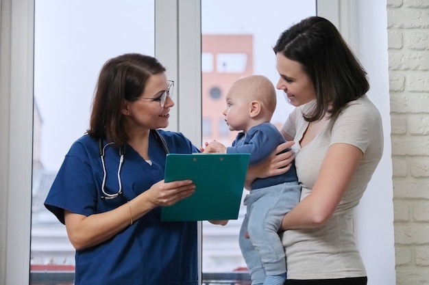 Médico pediatra hablando con la joven madre sosteniendo a su bebé en sus brazos