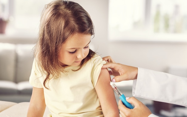 Médico pediatra haciendo la vacunación de una niña