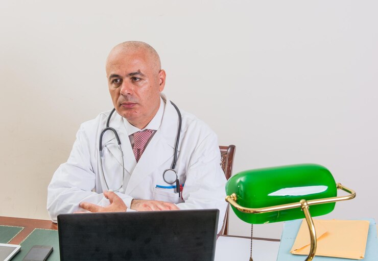 Foto médico pensativo sentado en el escritorio contra la pared blanca