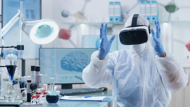 Médico pesquisador especialista usando fone de ouvido de realidade virtual, analisando a estrutura da atividade cerebral, fazendo gestos com as mãos durante experimento de bioquímica no laboratório de microbiologia. Conceito de medicina