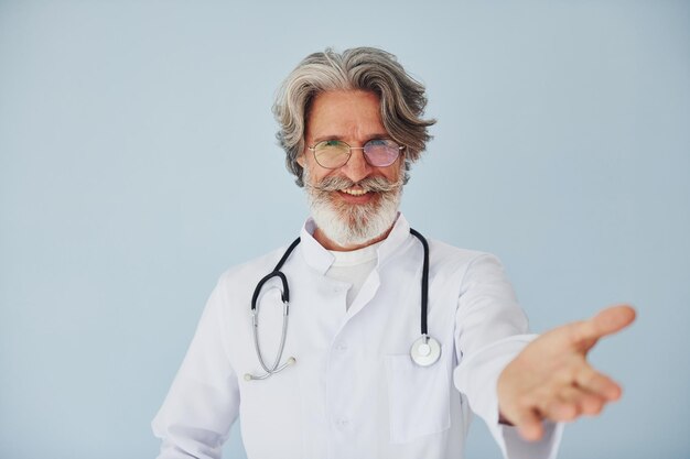 Médico positivo profesional Senior hombre moderno con estilo con cabello gris y barba en el interior