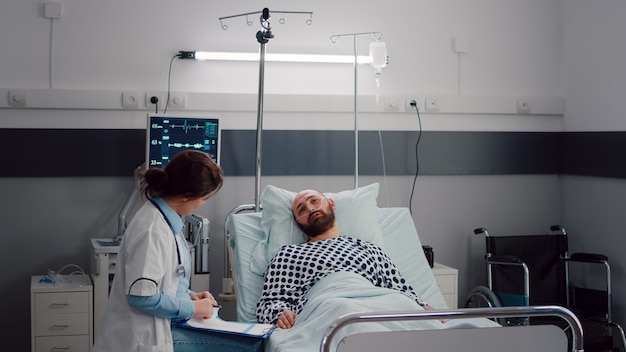 Médico practicante que supervisa al hombre enfermo escribiendo el tratamiento de la enfermedad en el portapapeles