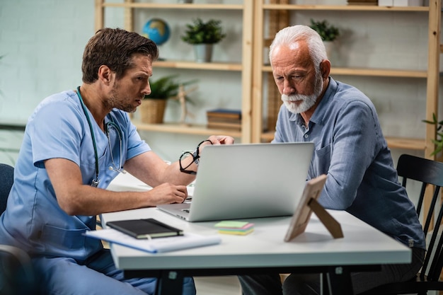 Médico preocupado e homem sênior usando laptop e discutindo sobre resultados de testes após exame médico