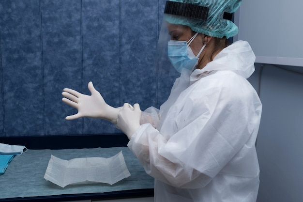 Un médico se prepara para atender a un paciente. La mujer prepara (trajes de protección, gafas, guantes y máscaras) todas las protecciones necesarias para protegerse del covid-19.