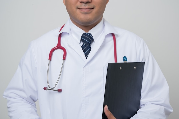 Médico de primer plano medio en bata blanca, estetoscopio sosteniendo el portapapeles al lado del brazo