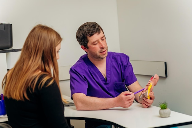 Médico proctologista masculino mostrando modelo artificial de reto humano para paciente no hospital durante consulta