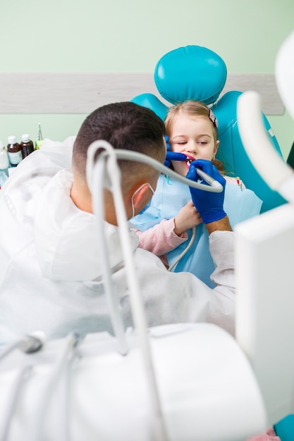 Un médico profesional, un dentista infantil, trata los dientes de una niña con instrumentos. Consultorio dental para examen de pacientes. El proceso de tratamiento dental en un niño.