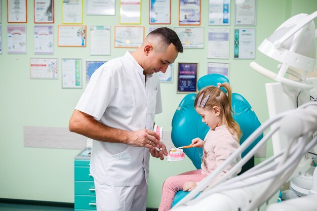 Médico profesional, dentista pediátrico enseña a un niño a cepillarse los dientes. Consultorio dental para examen de pacientes. El proceso de tratamiento dental en un niño.