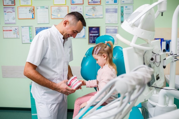 Médico profesional, dentista pediátrico enseña a un niño a cepillarse los dientes. Consultorio dental para examen de pacientes. El proceso de tratamiento dental en un niño.