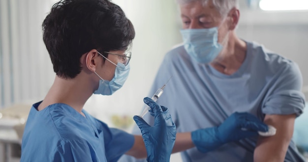 Médico profissional dando injeção de vacina covid19 para paciente sênior na clínica