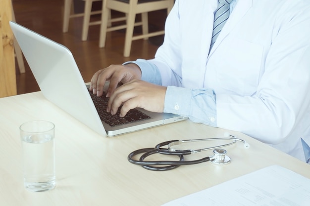 Médico profissional em vestido de uniforme branco vestido trabalhando laptop.