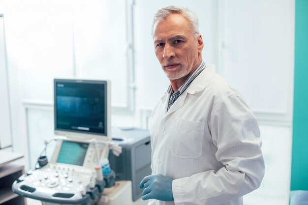 Médico profissional sério sozinho com um scanner de ultrassom ao fundo