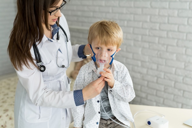 Médico que aplica el tratamiento de inhalación de medicamentos en un niño con terapia de inhalación para el asma por la máscara del inhalador.