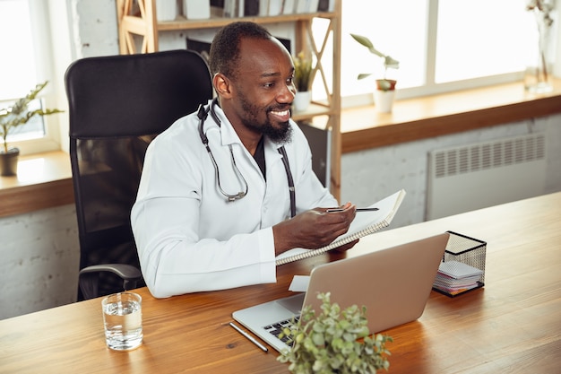 Médico que consulta al paciente, dando recomendación. Médico afroamericano durante su trabajo con pacientes, explicando recetas de medicamentos. Trabajo arduo diario para la salud y salvar vidas durante la epidemia.