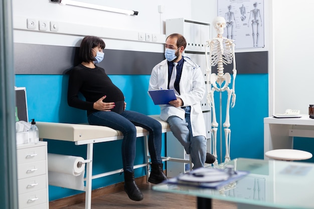Médico que consulta o adulto grávido na consulta médica. clínico geral e mulher grávida fazendo exame de check-up, discutindo sobre apoio ao parto no gabinete.