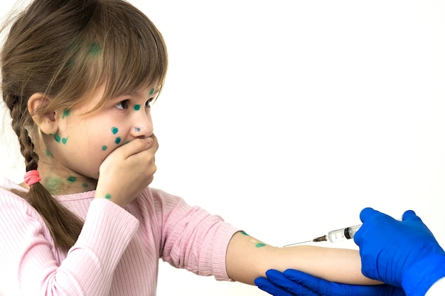 Médico que hace la inyección de la vacuna a una niña asustada enferma de varicela, sarampión o virus de la rubéola. La vacunación de los niños en el concepto de escuela.