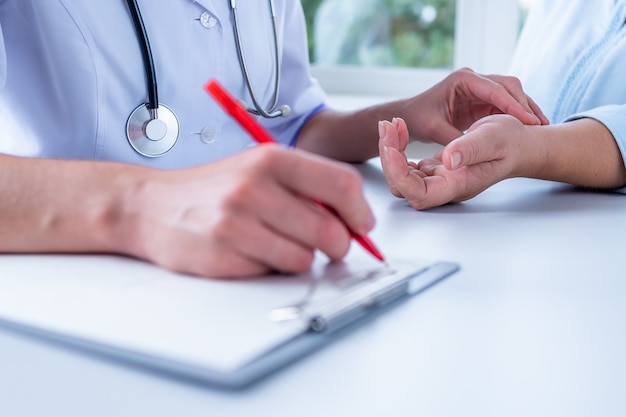 Médico que mide el pulso del paciente y escribe el diagnóstico y el tratamiento de la enfermedad durante un examen médico y consulta en el hospital