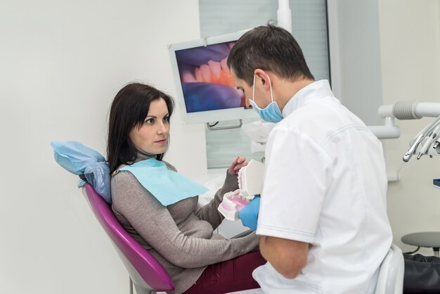 Médico que muestra al paciente cómo limpiar los dientes en la muestra de la mandíbula