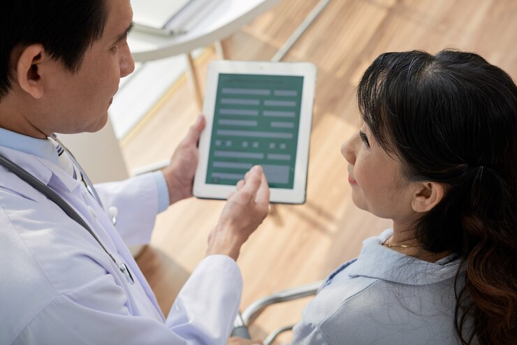 Foto médico que le pide al paciente mayor que complete la información personal en el formulario en la computadora de la tableta antes del examen