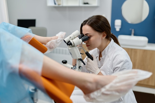 Foto un médico que realiza un examen ginecológico de una paciente en una silla con microscopio ginecológico