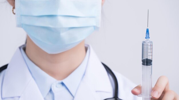 Médico que sostiene una jeringa con el concepto de máscara facial de una joven médica que inyecta la vacuna coronavirus COVID19 sobre fondo blanco cerca del espacio de copia