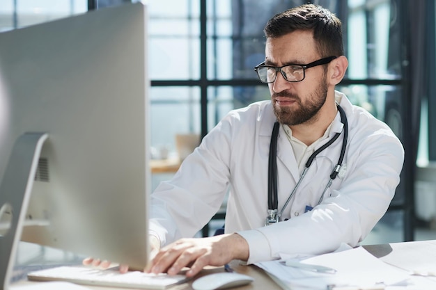 Foto médico que trabaja con una computadora portátil y escribe en el papeleo antecedentes del hospital