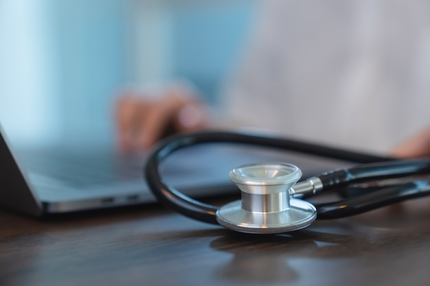 Foto el médico que usa la computadora en el escritorio en la oficina y el estetoscopio en la mesa.