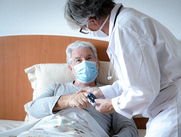 El médico que usa estetoscopio mide el oxígeno en la sangre de un anciano en la cama durante una visita a su hogar